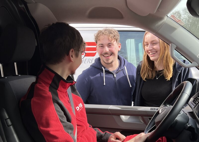 Ein Auszubildender sitzt in einem Servicetechniker-Wagen und lacht mit zwei anderen Auszubildenden, die außerhalb des Wagens stehen